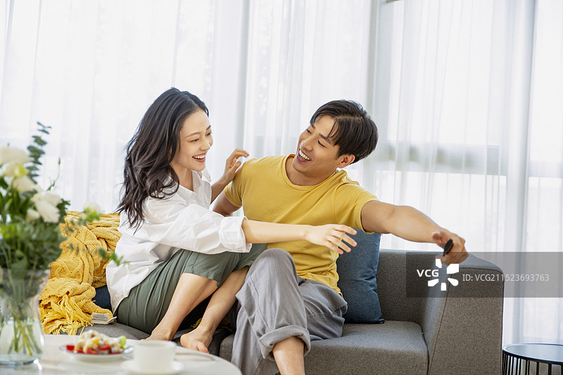年轻情侣在客厅看电视、争抢遥控器图片素材