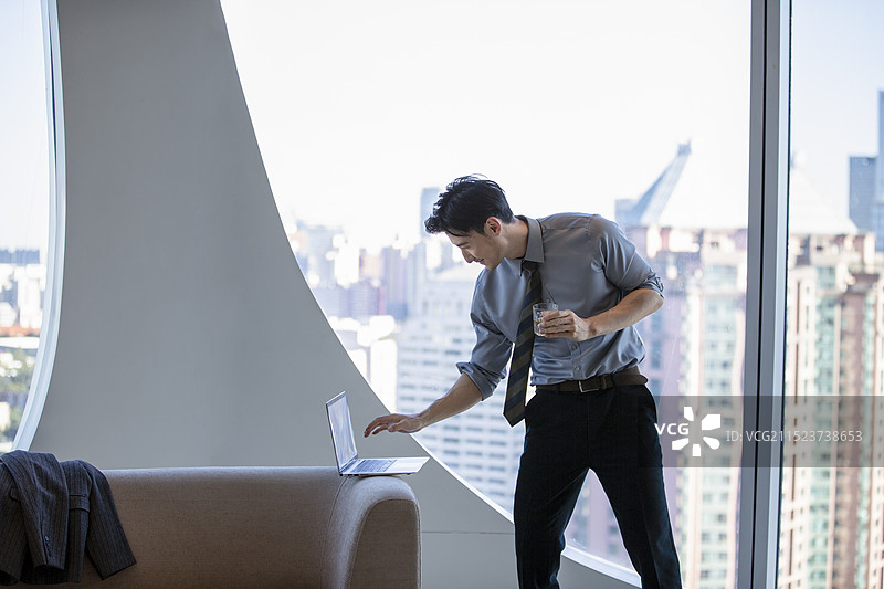 商务男子在酒店房间使用笔记本电脑、喝威士忌、跳舞图片素材