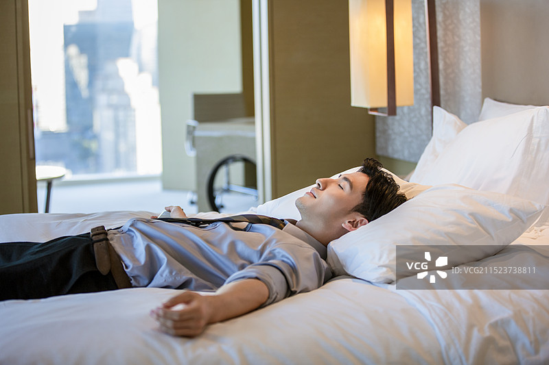 成熟的商务男子躺在酒店房间床上小睡图片素材