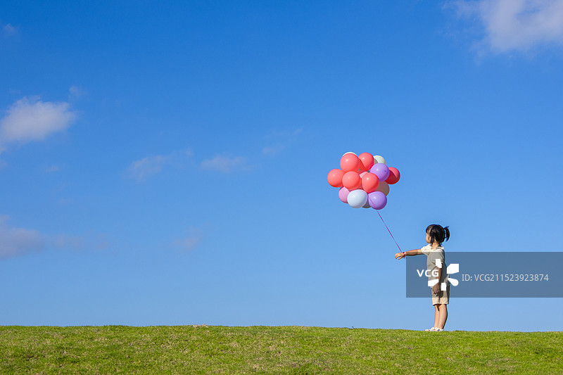 蓝天白云下小女孩在草地上玩气球图片素材