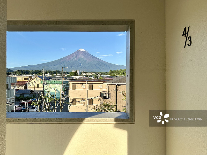 旅店走廊窗户框架下清晨富士山和日本城市，山顶飘过一朵云图片素材