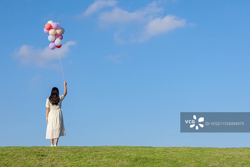 草地上一名拿着一束气球的中国女人背影图片素材