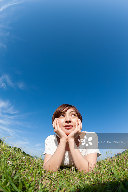 女人在草地上抬头看天空，露出颧骨图片素材