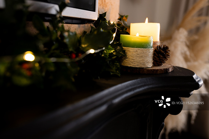 圣诞节，节日蜡烛在壁炉架上闪烁，装饰着冬青树和松果图片素材