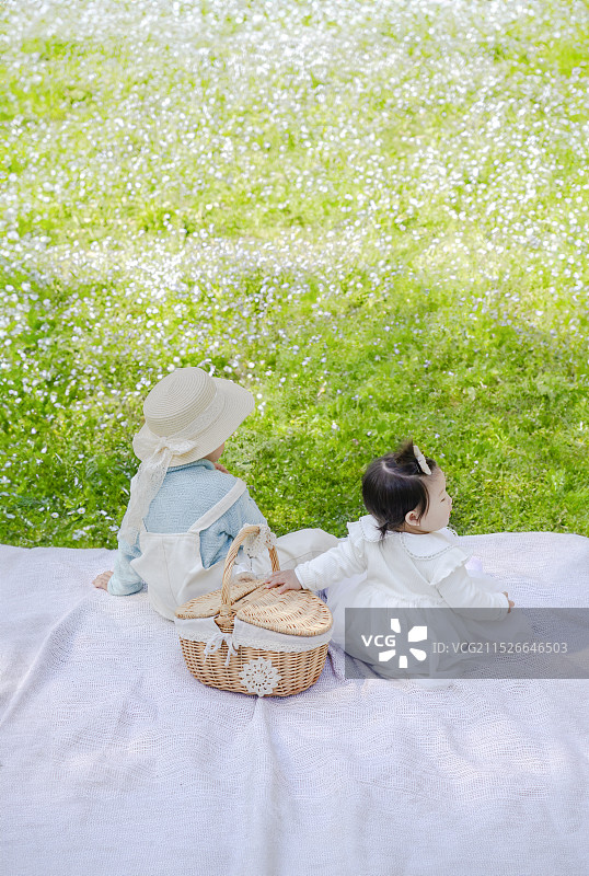 野外遍地鲜花丛草坪处休闲享受的女婴与小男孩背身视角图片素材