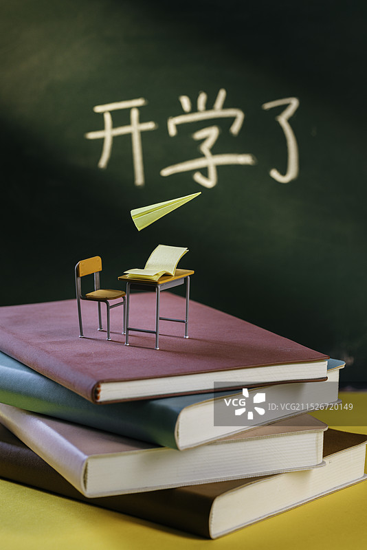 一摞书上的微缩课桌和背景里的黑板写着开学了图片素材