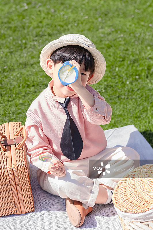 坐在草坪上手拿棒棒糖看万花筒的时尚男孩图片素材