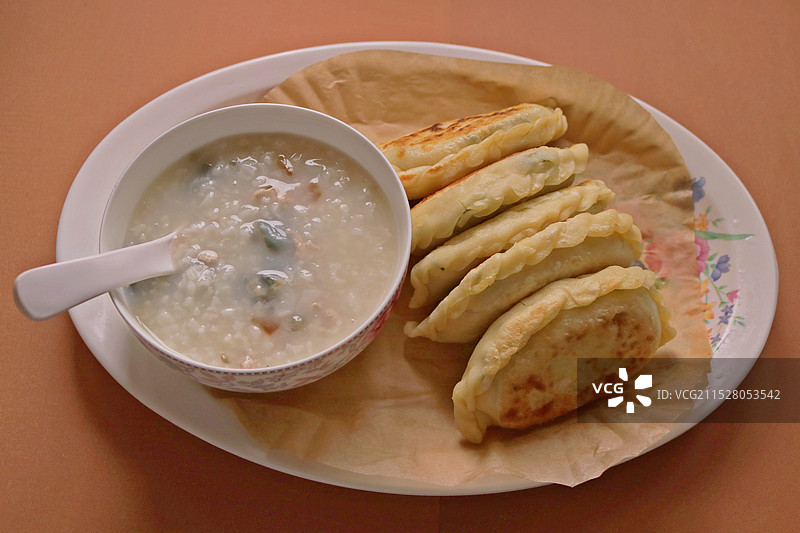 放在大盘子里的一碗皮蛋瘦肉粥和五个馅饼图片素材