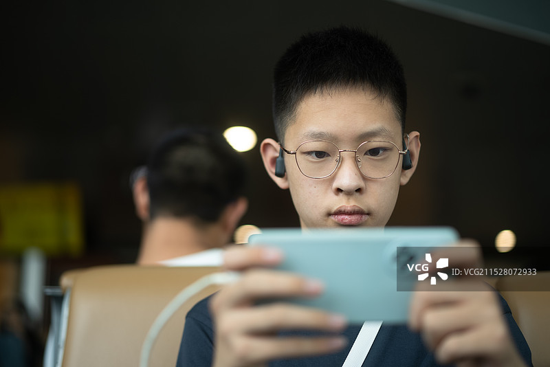 男孩在机场玩手机游戏图片素材