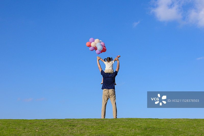 草地上玩气球的小女孩坐在爸爸肩膀上背影图片素材