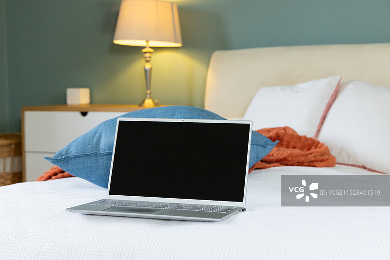 笔记本电脑放在温馨的卧室舒适的床上，准备在家工作，留有空白空间图片素材