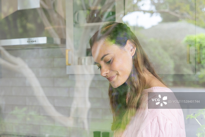 微笑的女性穿着舒适的毛衣，在窗边享受宁静的时光图片素材