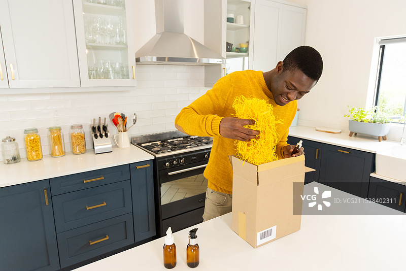 非裔美国男性在厨房拆礼物盒，面带兴奋和快乐的微笑，身处家中图片素材