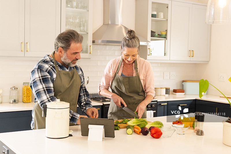 在现代厨房准备健康餐的成熟夫妇，微笑着在家中。图片素材