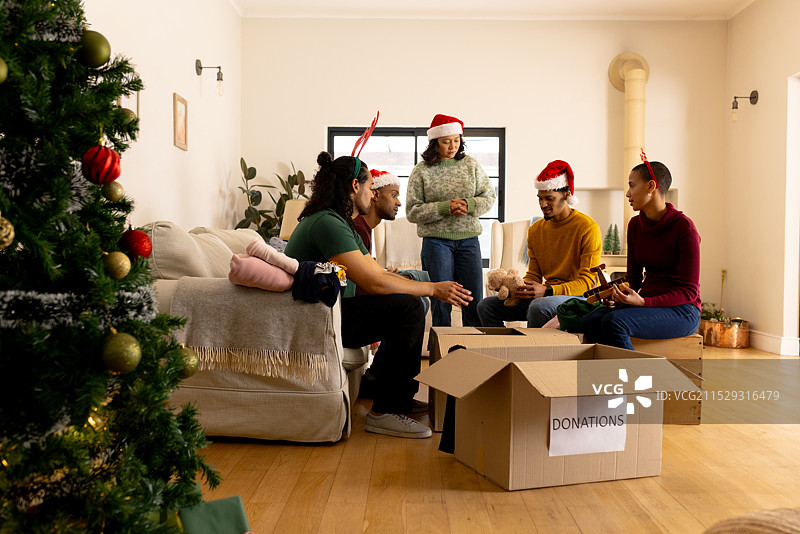 年轻的多种族朋友们戴着圣诞帽在家一起整理节日捐赠物品图片素材