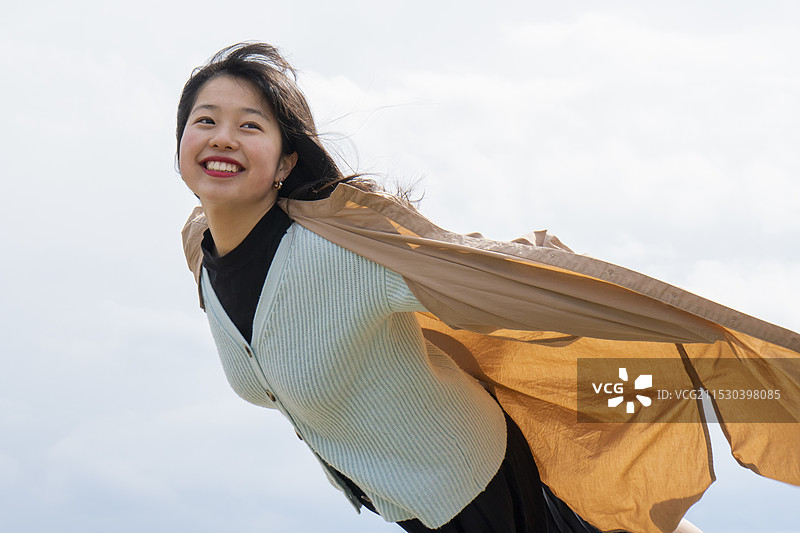 女人高兴地发现她的外套在风中蓬松起来，感觉像是在空中飞翔。图片素材