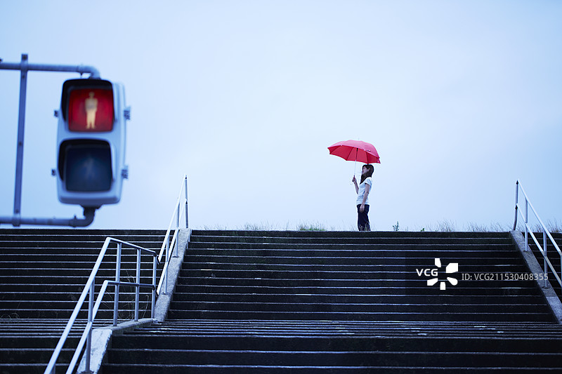 女人站在河岸的台阶前，手持雨伞。图片素材