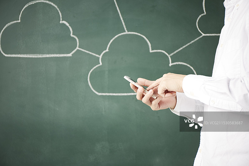 一个人在黑板前触摸智能手机，周围有几个连接的云朵。图片素材