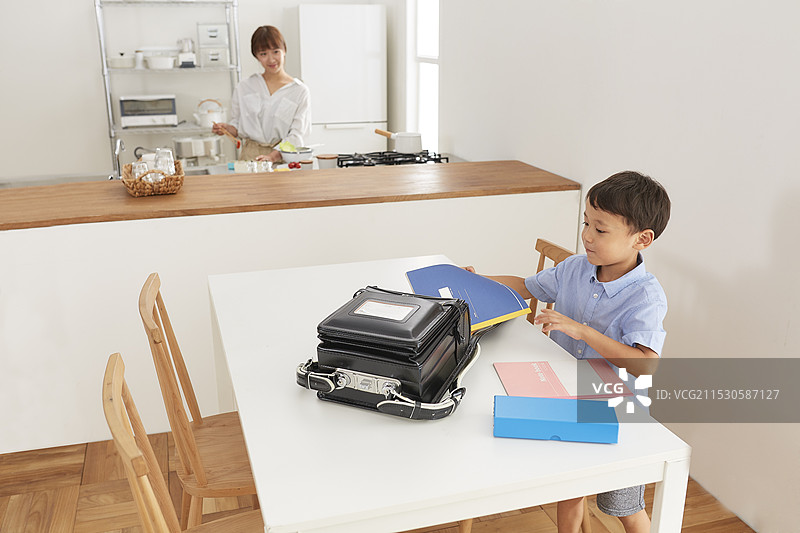 女人在厨房准备午餐，男孩在餐厅为上学做准备。图片素材