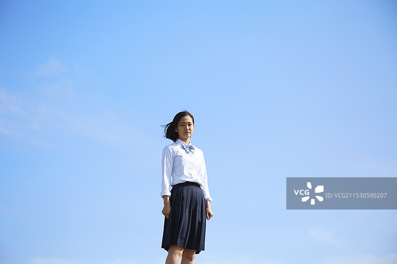 高中女孩在蓝天下朝镜头看。图片素材