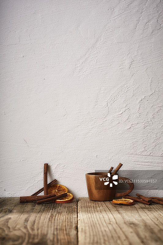 木制杯子里放着肉桂棒和干橙子，摆放在木质桌面上图片素材