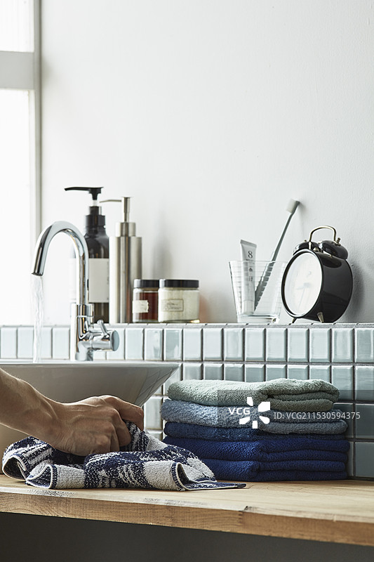 白色墙壁和浅蓝色瓷砖洗手盆，男人的手正在抓毛巾图片素材