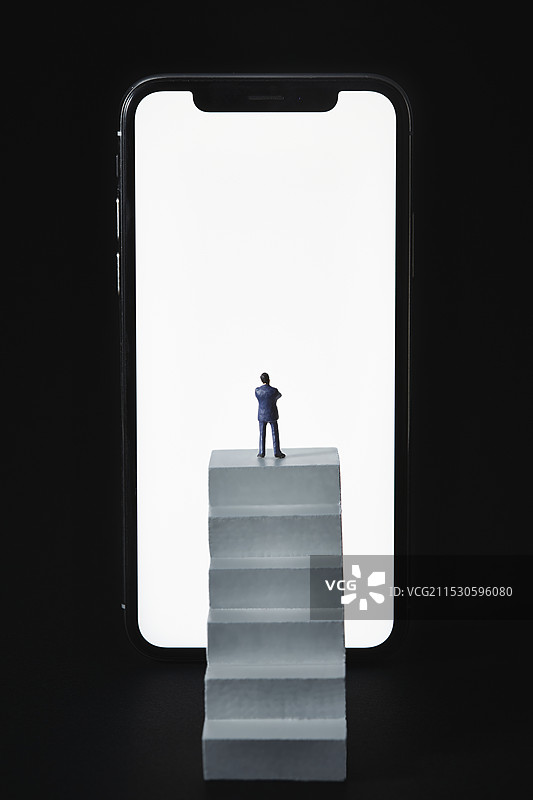 迷你玩偶与智能手机屏幕前的小楼梯图片素材