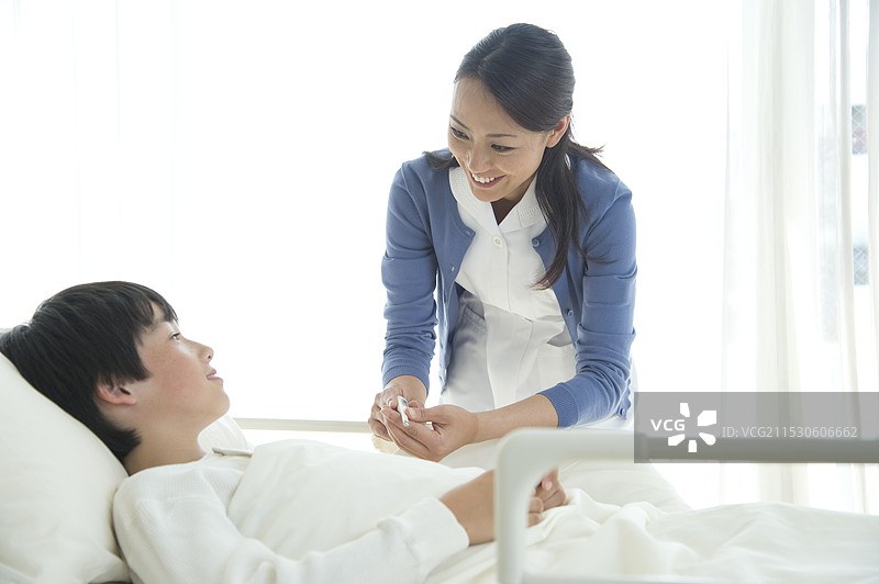 护士将温度计递给躺在病床上的男孩图片素材