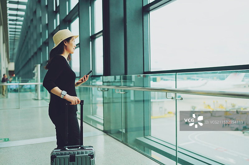 携带行李和智能手机在机场窗口等候的旅客图片素材