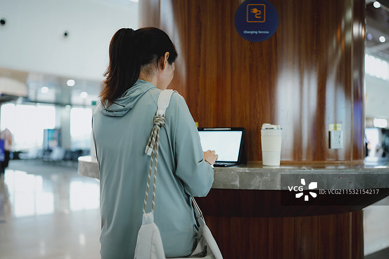 在现代咖啡馆环境中使用手机和笔记本电脑的年轻女性图片素材