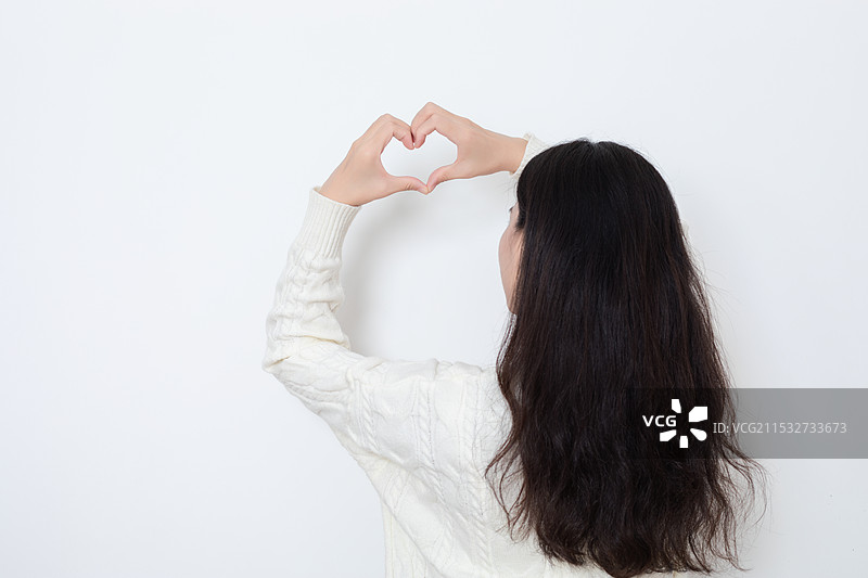 白墙前一位长发美女做出爱心手势图片素材