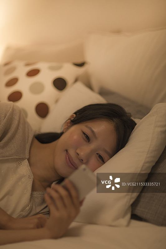 女人躺在床上看智能手机图片素材