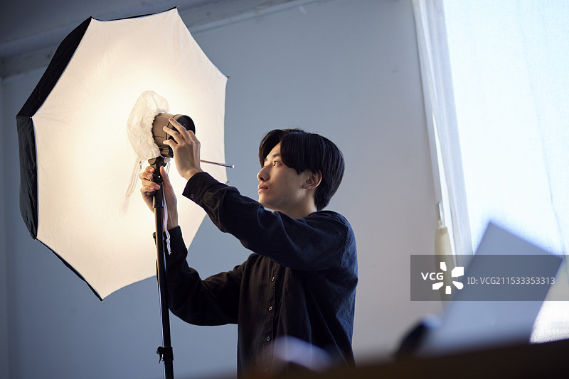 一位日本男性摄影师在摄影工作室调整闪光灯。图片素材