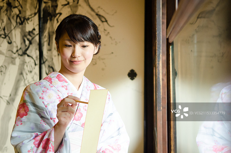 穿着和服的女性用毛笔在短册上写俳句图片素材