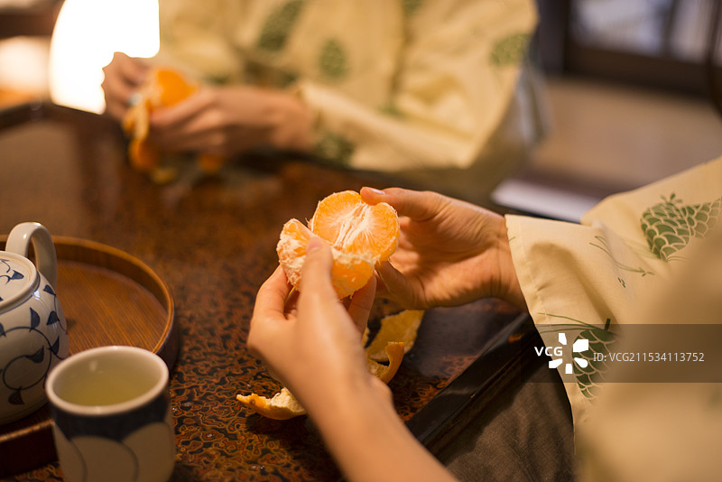两位女性在火炉桌上剥橙子图片素材
