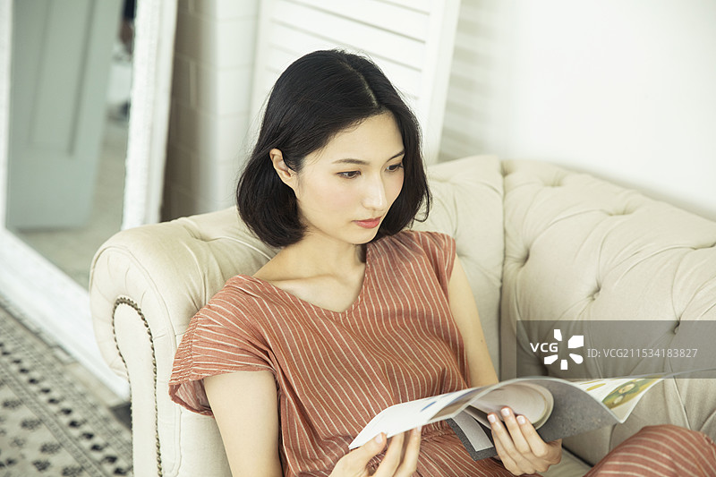 20多岁的女性坐在沙发上阅读杂志图片素材