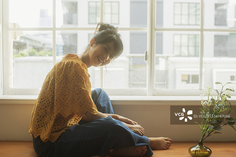 20多岁的微笑女性在窗边放松图片素材