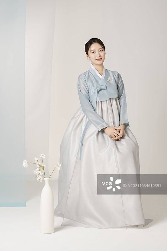 一位美丽的女性穿着华丽优雅的韩服，坐在一个花瓶旁边。图片素材