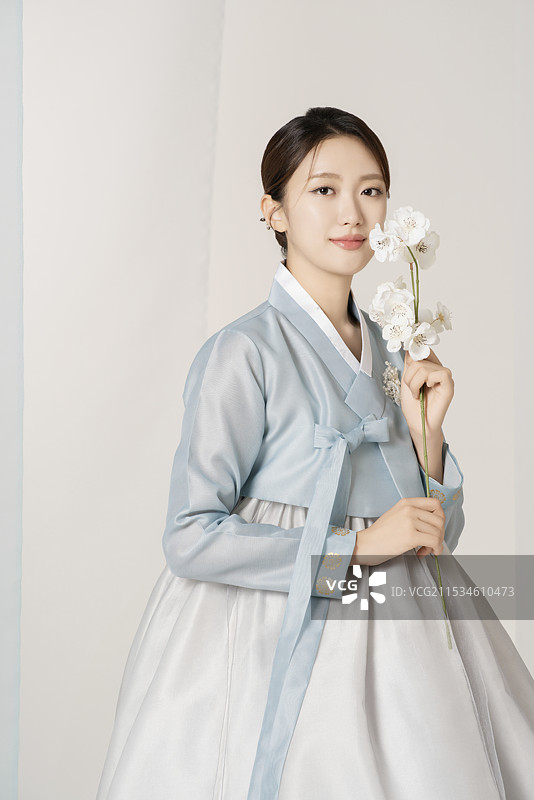 一位美丽的女性穿着华丽优雅的韩服，手中捧着一朵花。图片素材