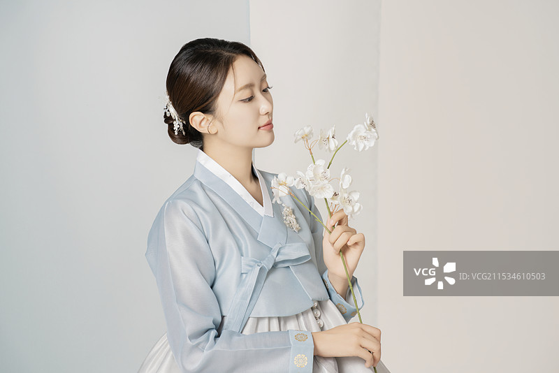 一位美丽的女性穿着华丽优雅的韩服，手中捧着一朵花。图片素材