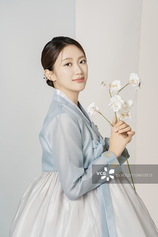 一位美丽的女性穿着华丽优雅的韩服，手中捧着一朵花。图片素材