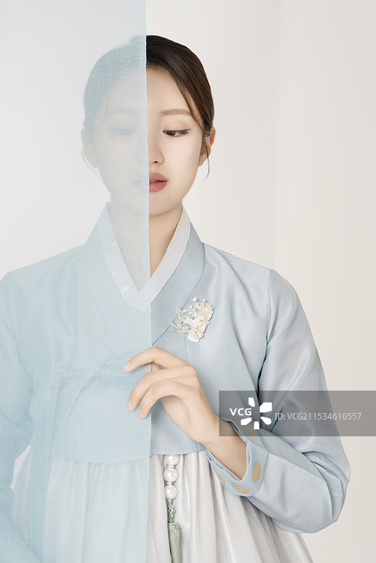 一位美丽的女性穿着华丽优雅的韩服，站在蓝色布料后面图片素材