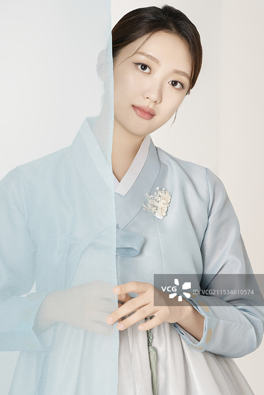 一位美丽的女性穿着华丽优雅的韩服，站在蓝色布料后面图片素材