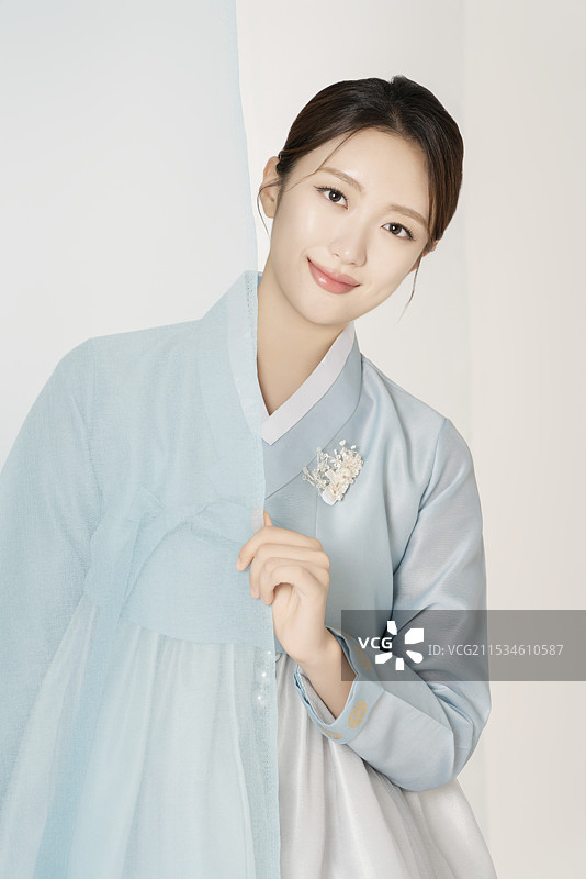 一位美丽的女性穿着华丽优雅的韩服，站在蓝色布料后面图片素材