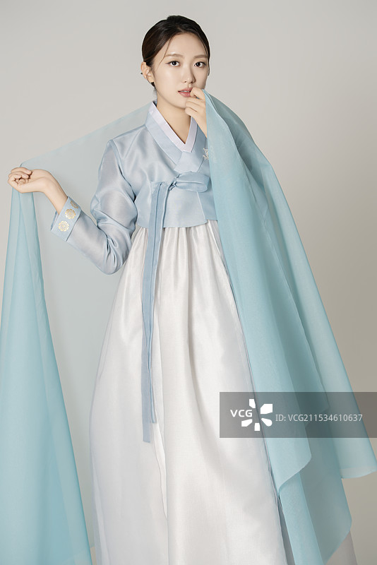 一位美丽的女性穿着华丽优雅的韩服，站在蓝色布料的掩映下。图片素材