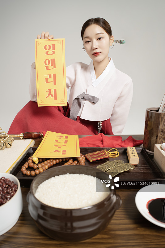 一位穿着韩服的萨满坐着，手中握着护身符。图片素材