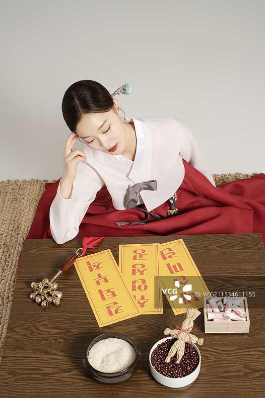 一位年轻的萨满穿着韩服，桌上摆放着萨满工具，正在思考。图片素材