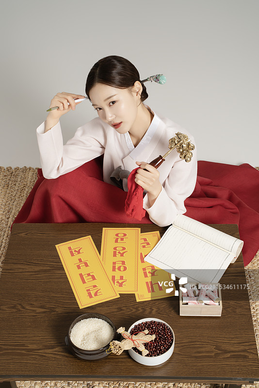 一位年轻的萨满穿着韩服，手持萨满铃，坐着沉思。图片素材