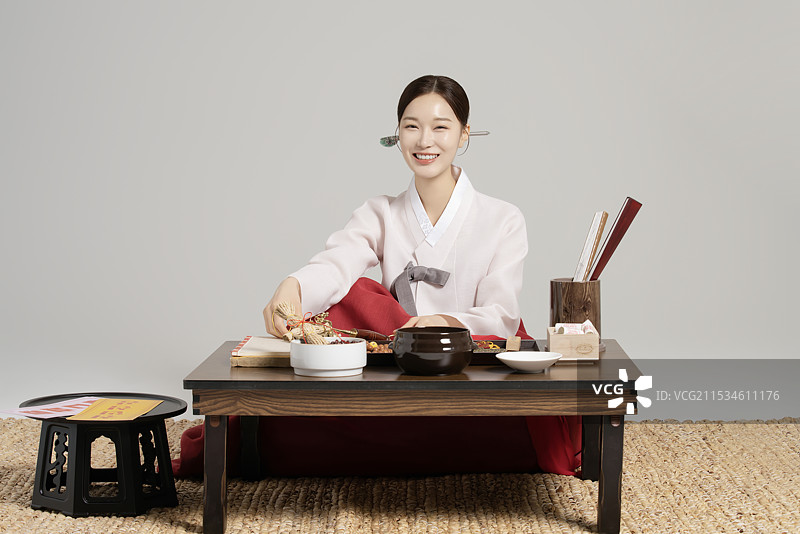 一位年轻的萨满穿着韩服，坐在桌子前，桌上摆放着萨满工具。图片素材