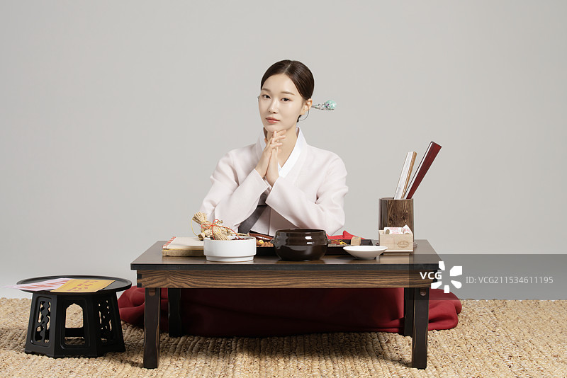 一位年轻的萨满穿着韩服，坐在桌子前，桌上摆放着萨满工具。图片素材